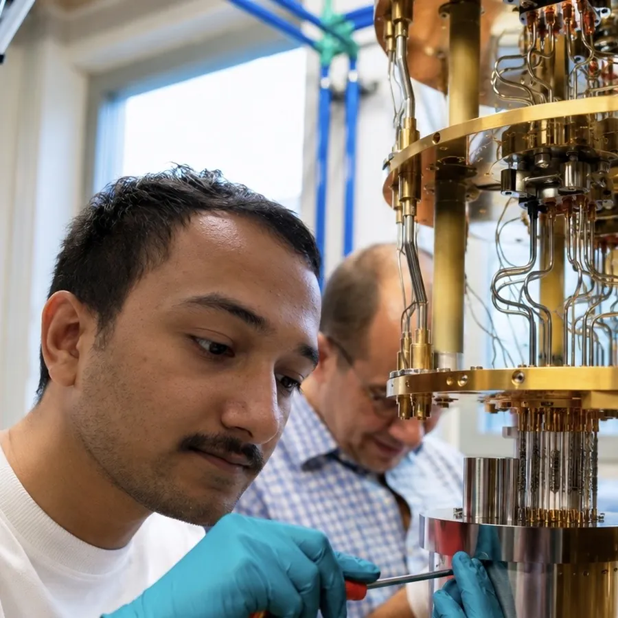 Souvik Ghosh in gloves working on the lower stages of a dilution refrigerator, a colleague behind him.