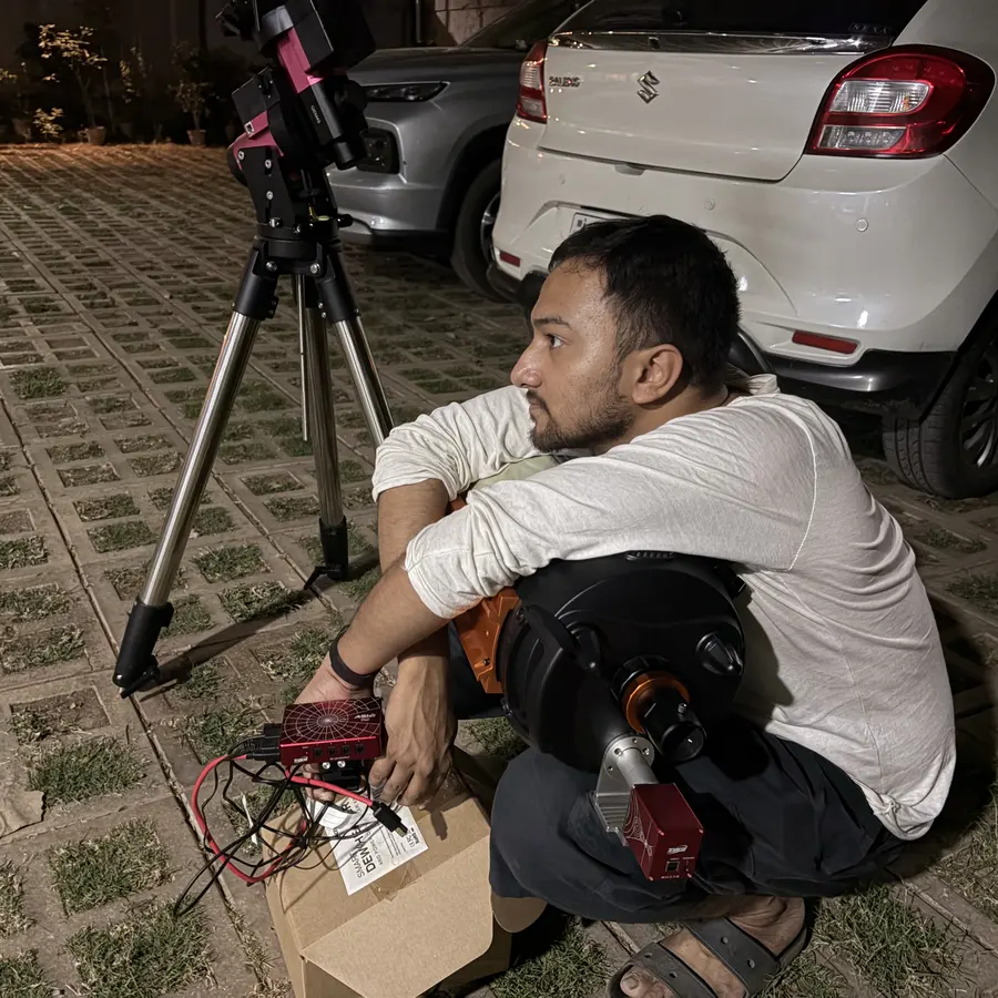 Souvik Ghosh sitting outdoors at night beside a tripod and observing gear.