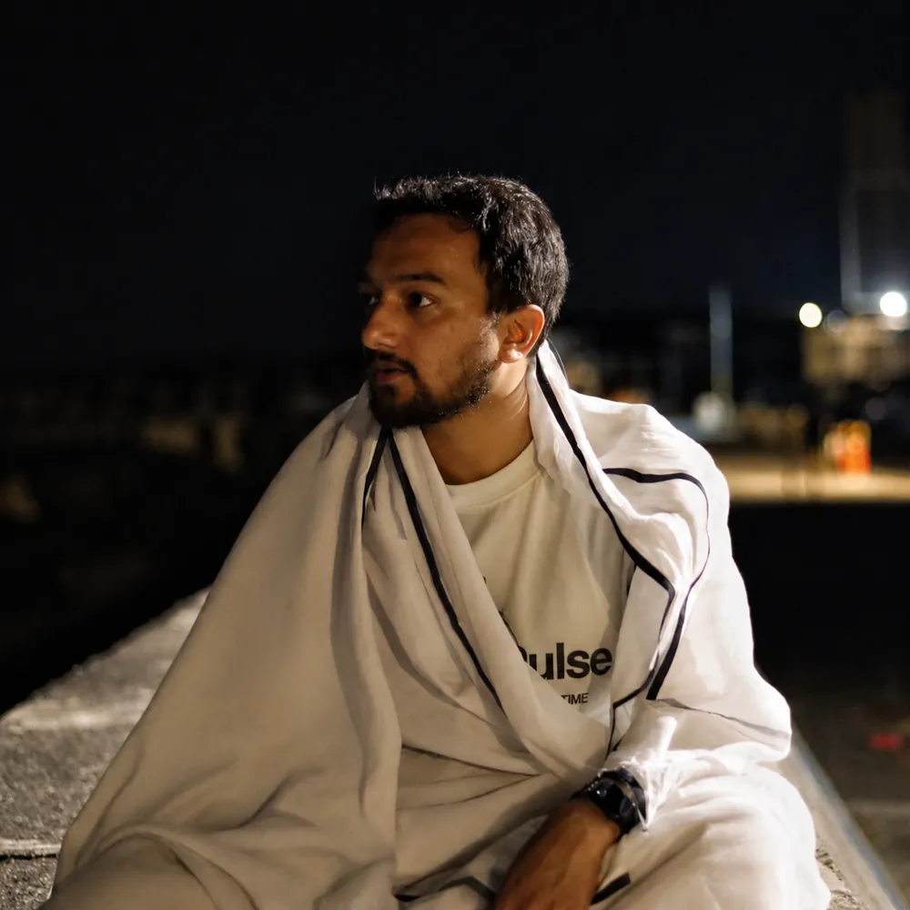 Souvik Ghosh at night on a rooftop, wrapped in a white shawl, looking out over the city lights.