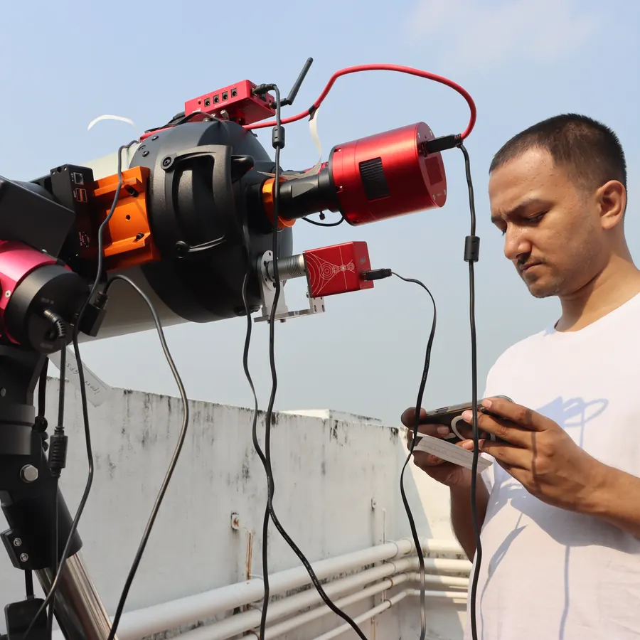 Souvik Ghosh on a rooftop beside the Purākaash telescope, holding its hand controller.