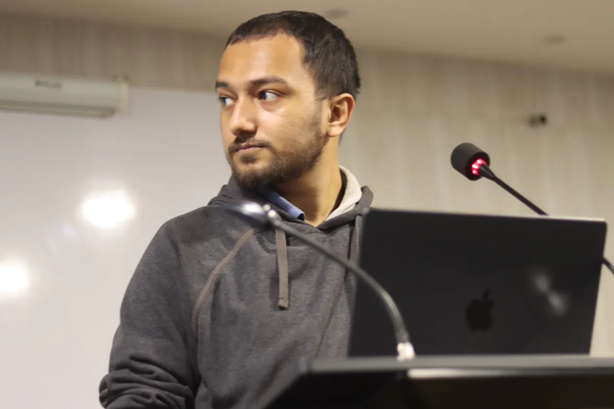 Souvik Ghosh speaking at a podium with a laptop, in front of a whiteboard.