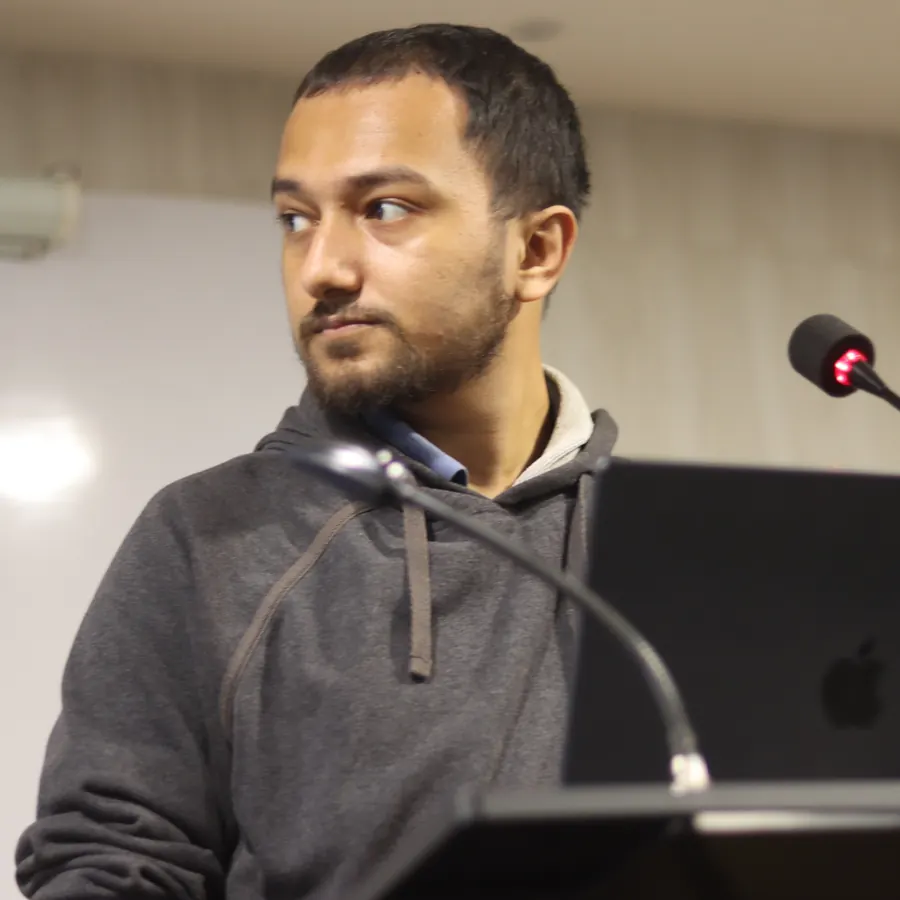 Souvik Ghosh at a podium with a laptop, in a grey hoodie, looking towards the audience.