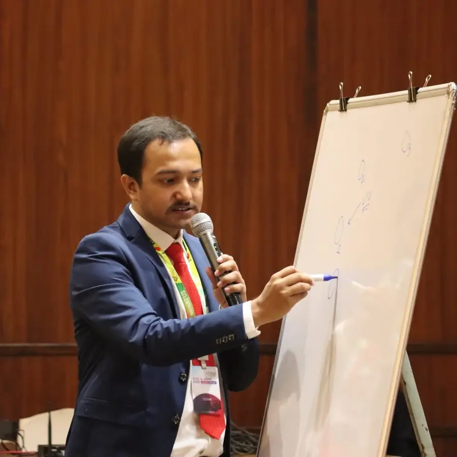 Souvik Ghosh in a suit, speaking into a microphone and writing on a whiteboard.