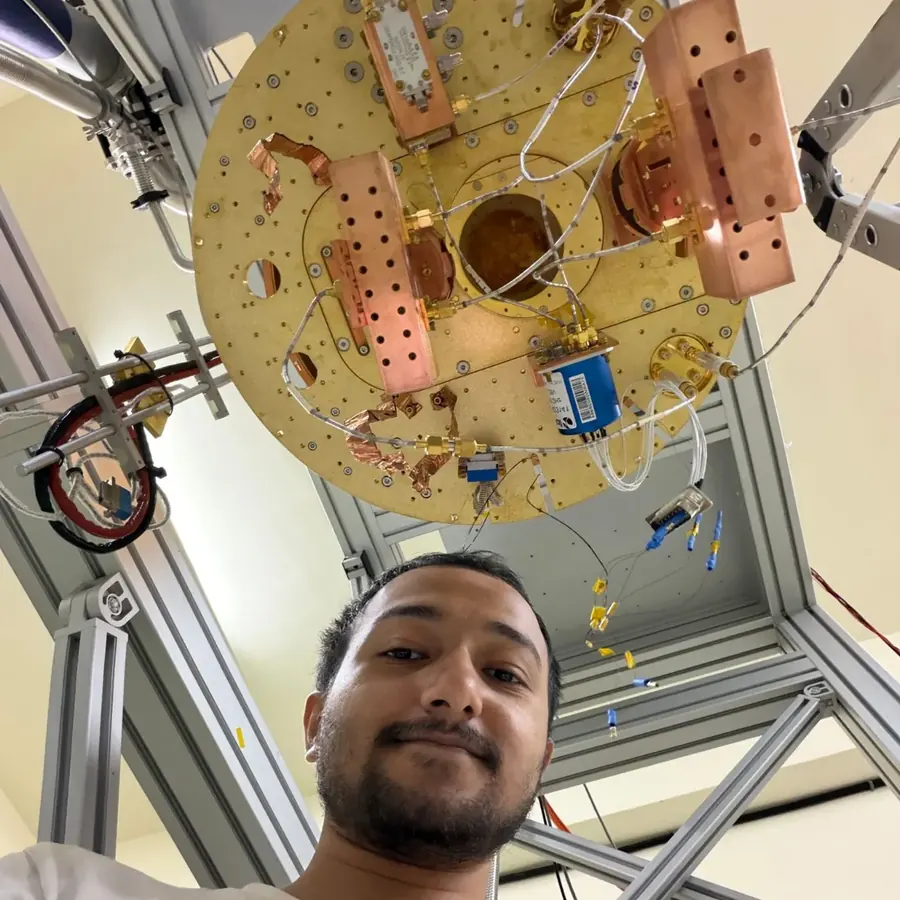 Souvik Ghosh looking up at the camera from under the lowest plate of a dilution refrigerator.
