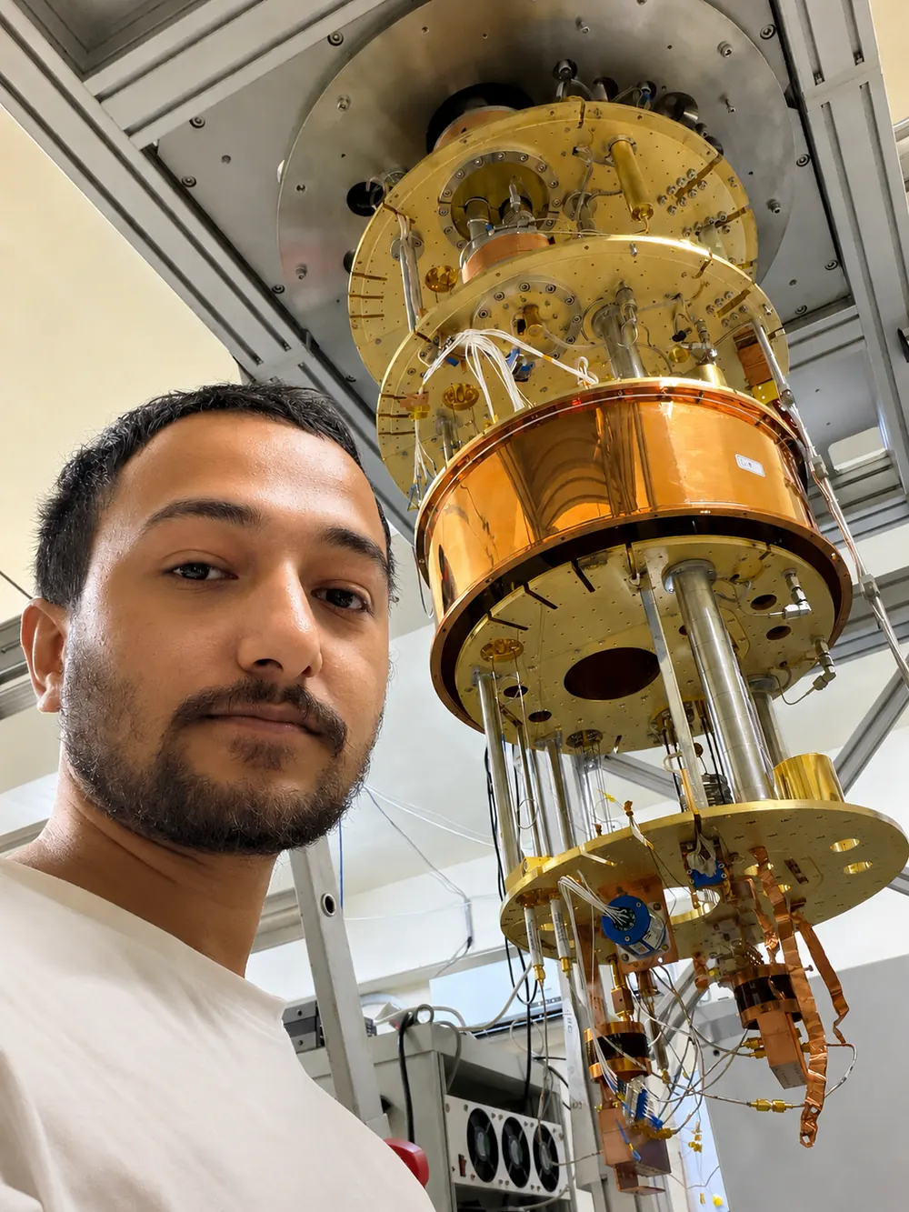 Souvik Ghosh beside an open dilution refrigerator: gold-plated plates stacked one below another, hung with wiring and copper parts.