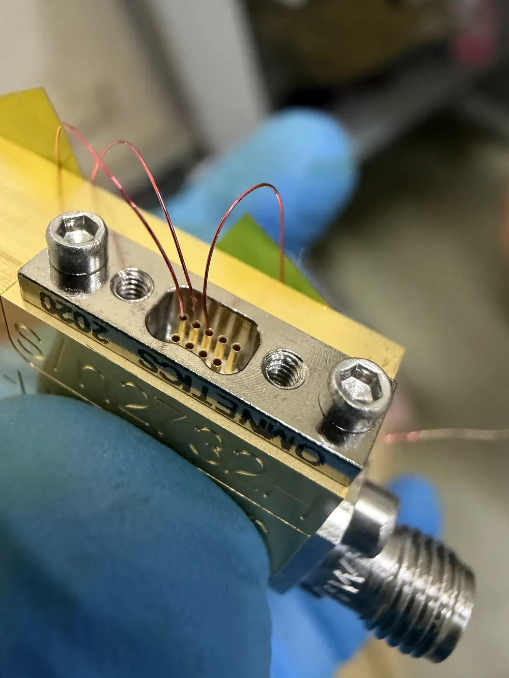 Close-up of a gold-plated sample holder with fine red copper wires looped into a small multi-pin connector.