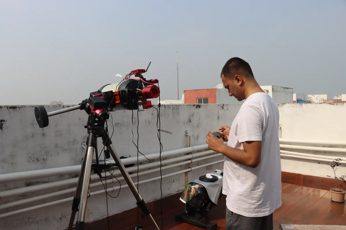 The telescope on its tripod on a rooftop in daylight, Souvik Ghosh standing beside it with the controller.